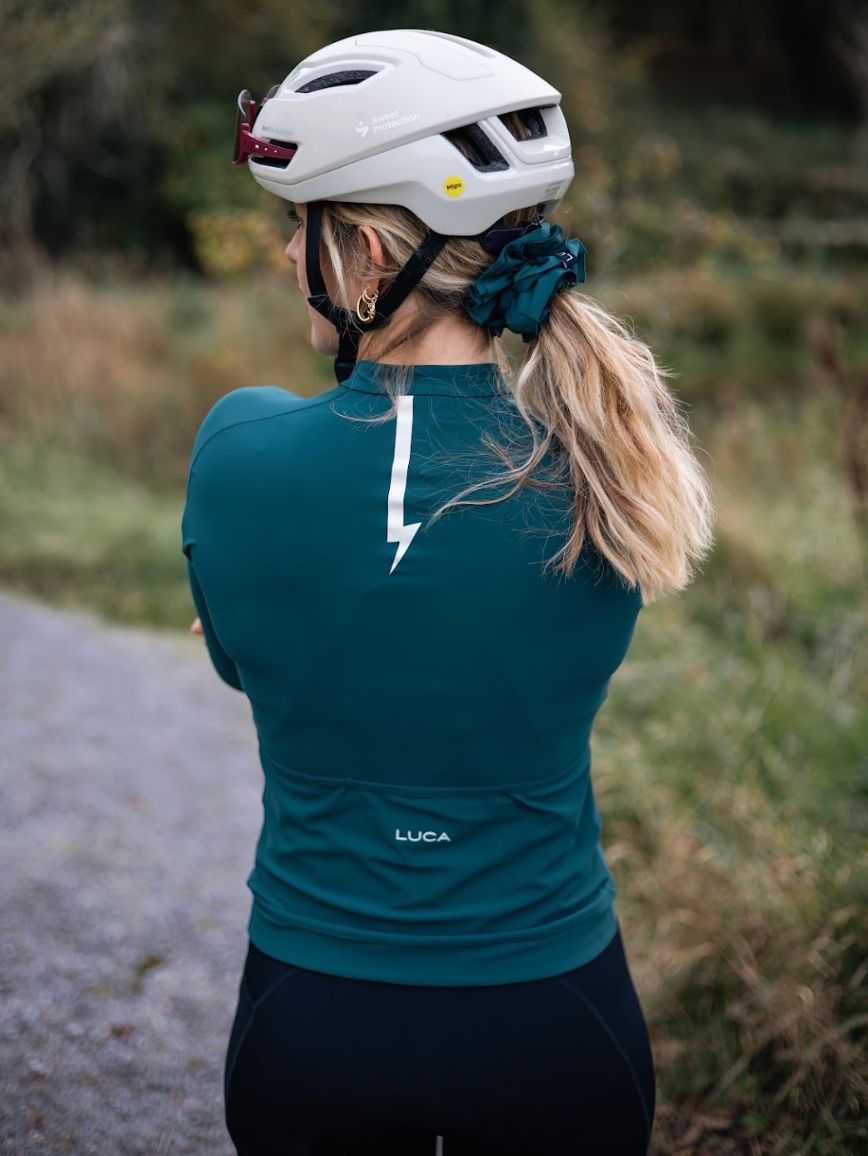 Back-view-of-a-cyclist-wearing-a- teal-long-sleeve-cycling-jersey-with- a-white-lightning-bolt-graphic-and- the-LUCA-logo-above-the-pocket.