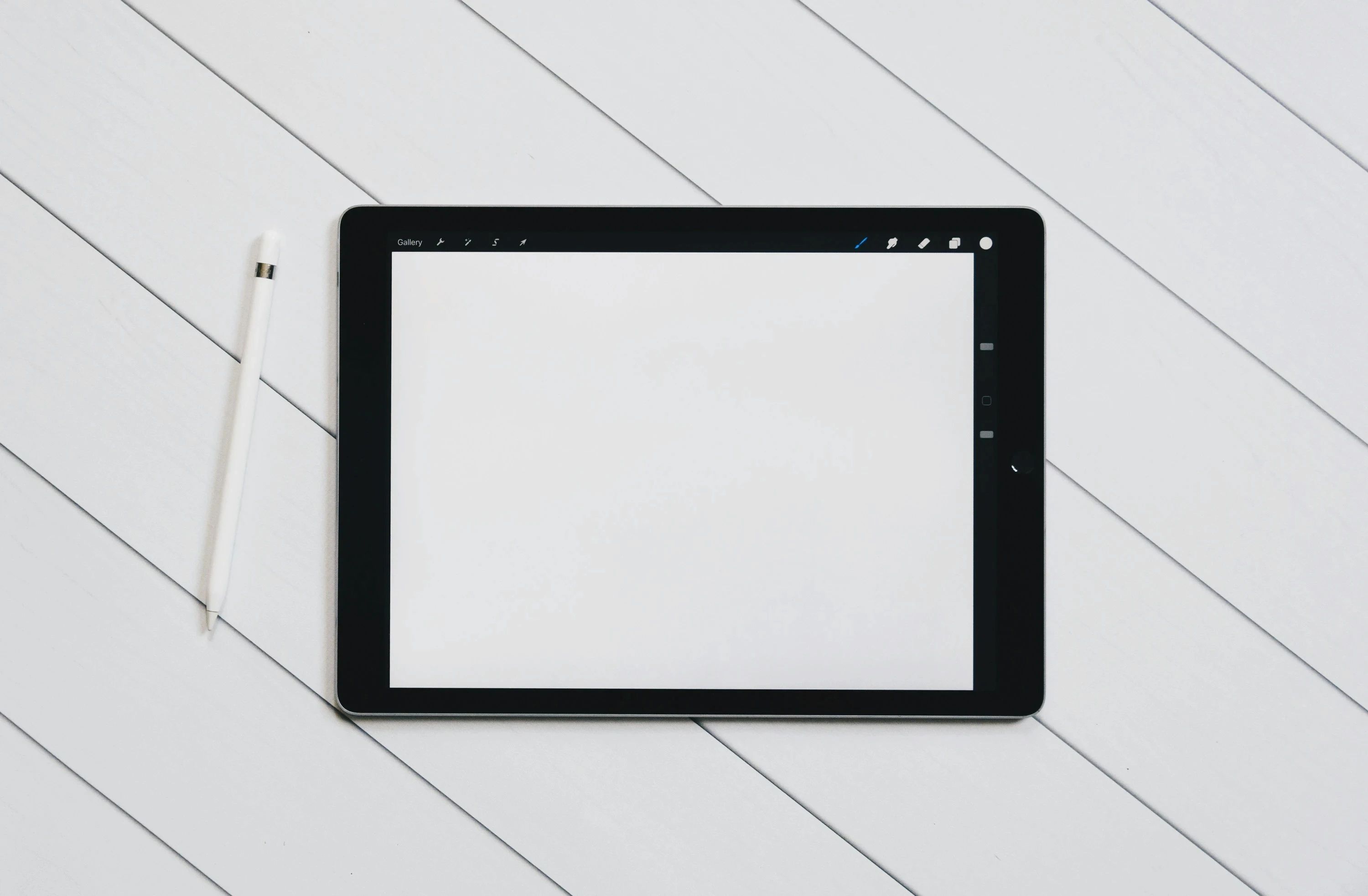 iPad with Apple Pencil on a white wooden floor, screen turned off and centered in frame.