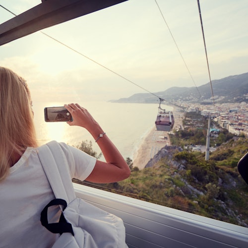 Traveling by Turkey. Young tourist woman sitting in Alanya's cable car enjoying view taking photos on her smartphone.