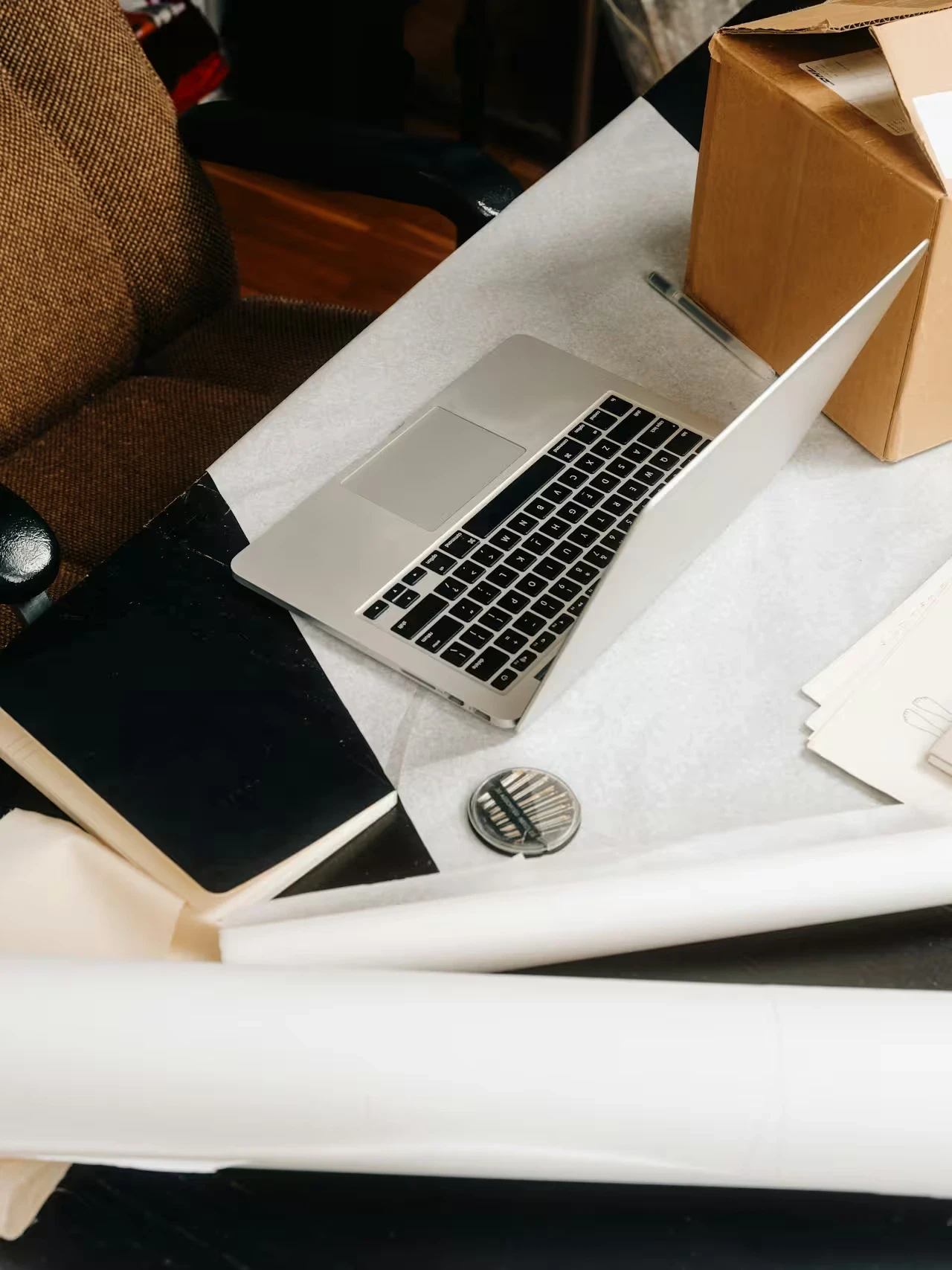 A laptop sits open among tissue paper, a cardboard box, and packing materials on a table.