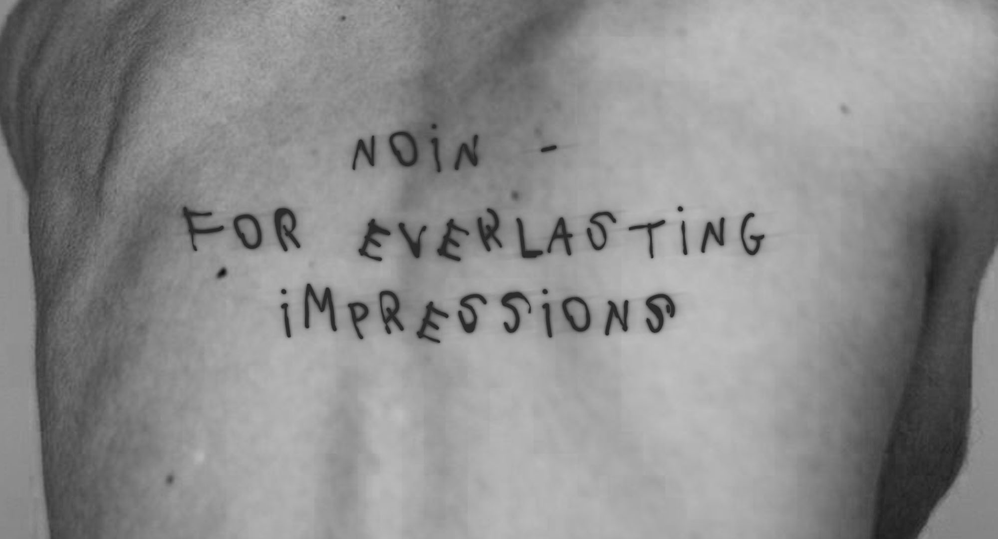 A black and white photo of a person with curly hair sitting on a chair in a barren, textured landscape.