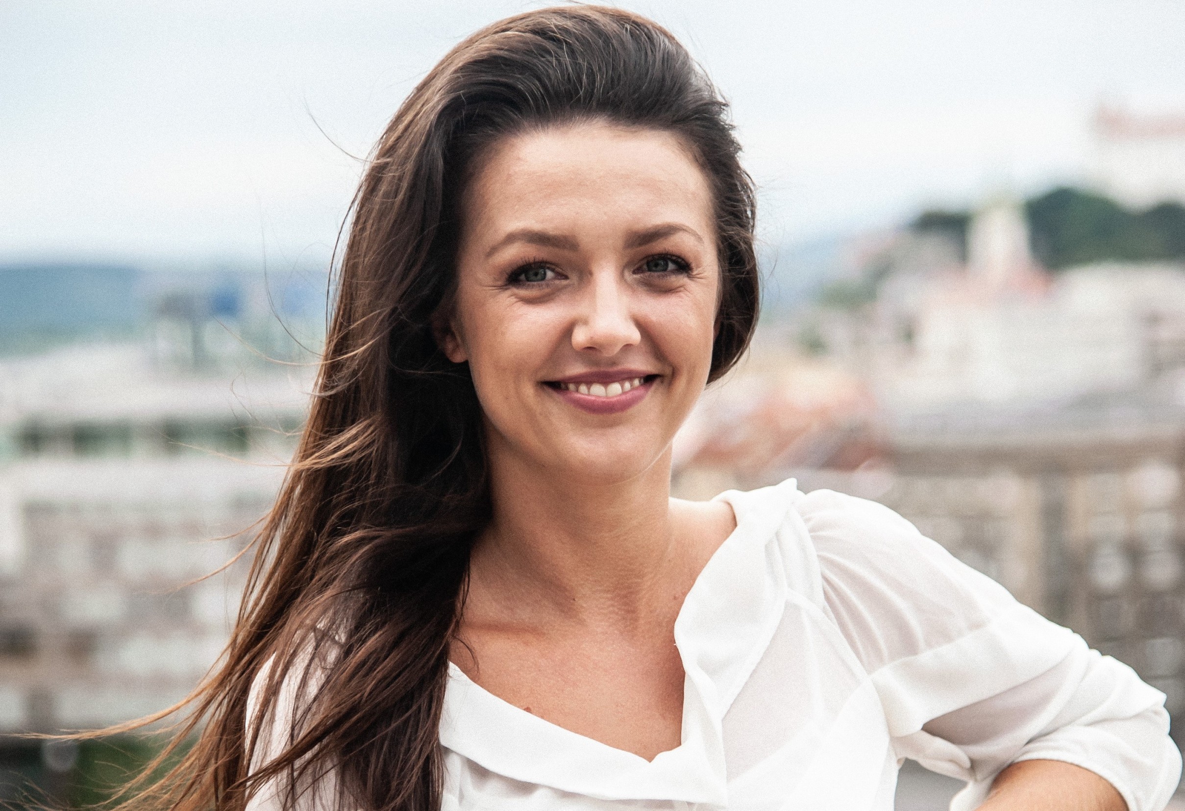 A woman with a white headband relaxing, her face illuminated by warm sunlight filtering through blinds, casting striped shadows. She has a serene and peaceful expression.