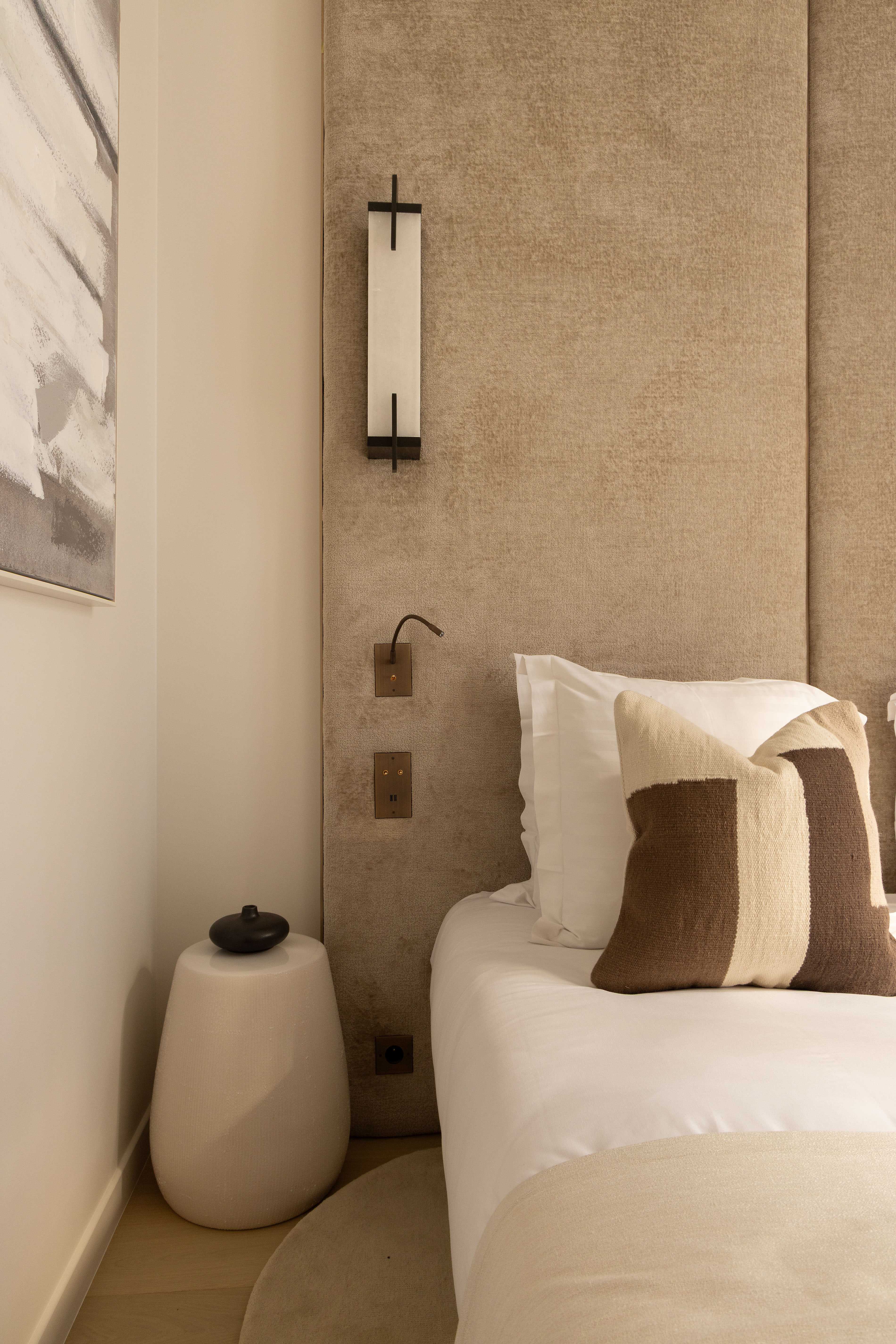 Détail chambre avec table de chevet ronde, applique murale et coin de tableau