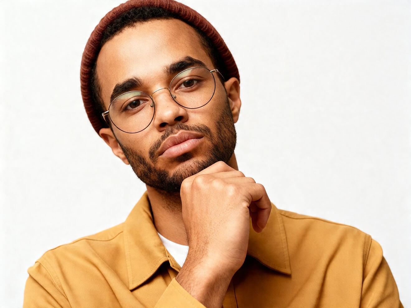 Close-up profile of a young designer wearing glasses and a burgundy beanie, with a calm expression against a soft neutral background.