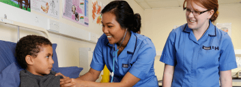 Nurses interacting with child patient in hospital room.