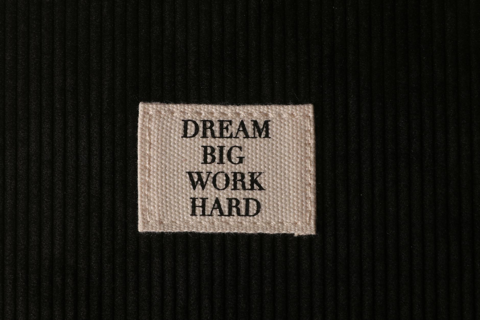 Close-up of patch with 'Dream Big, Work Hard' text on textured black fabric.