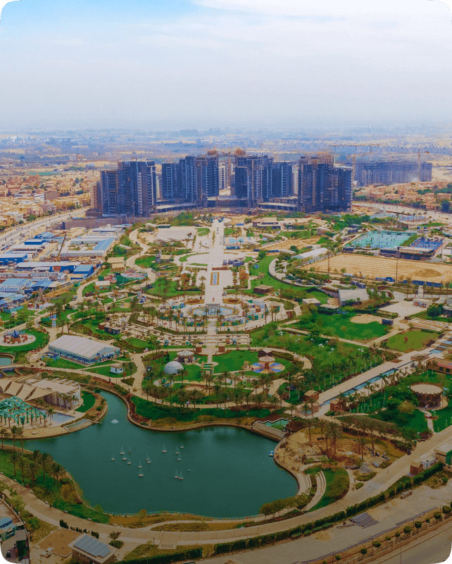 Aerial view of a landscape featuring water bodies, greenery, and modern buildings in the background.