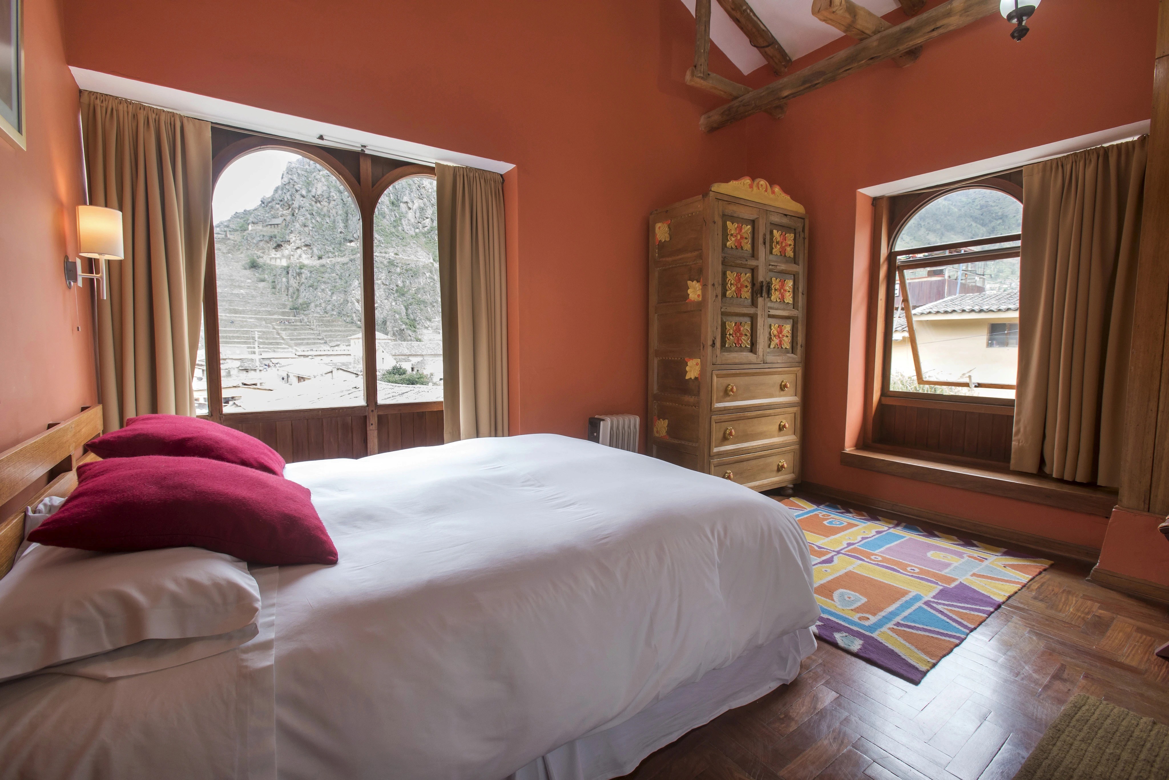 Bright bedroom with orange walls, a large window viewing mountains, and a rustic wooden cabinet.