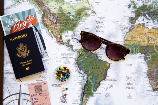Close-up of a passport, sunglasses, and a map spread out on a surface, suggesting travel preparations.