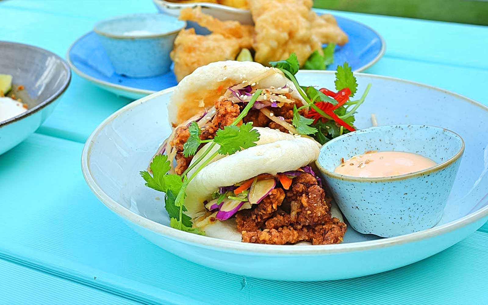 Gourmet bao buns with crispy filling and dipping sauce on a blue plate.