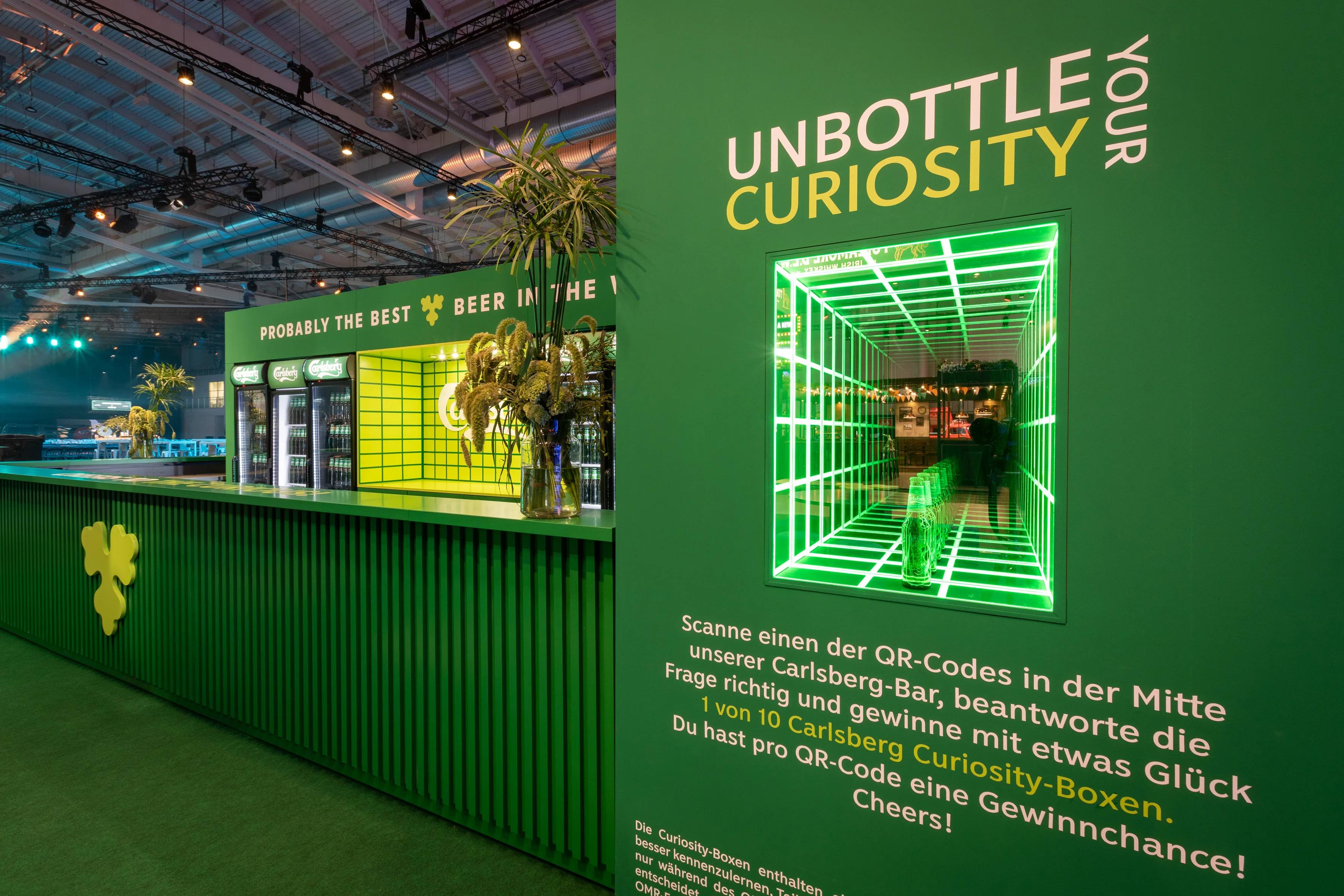 Unbottle Your Curiosity wall with infinity-mirror box of glowing green light frames at the Carlsberg booth.