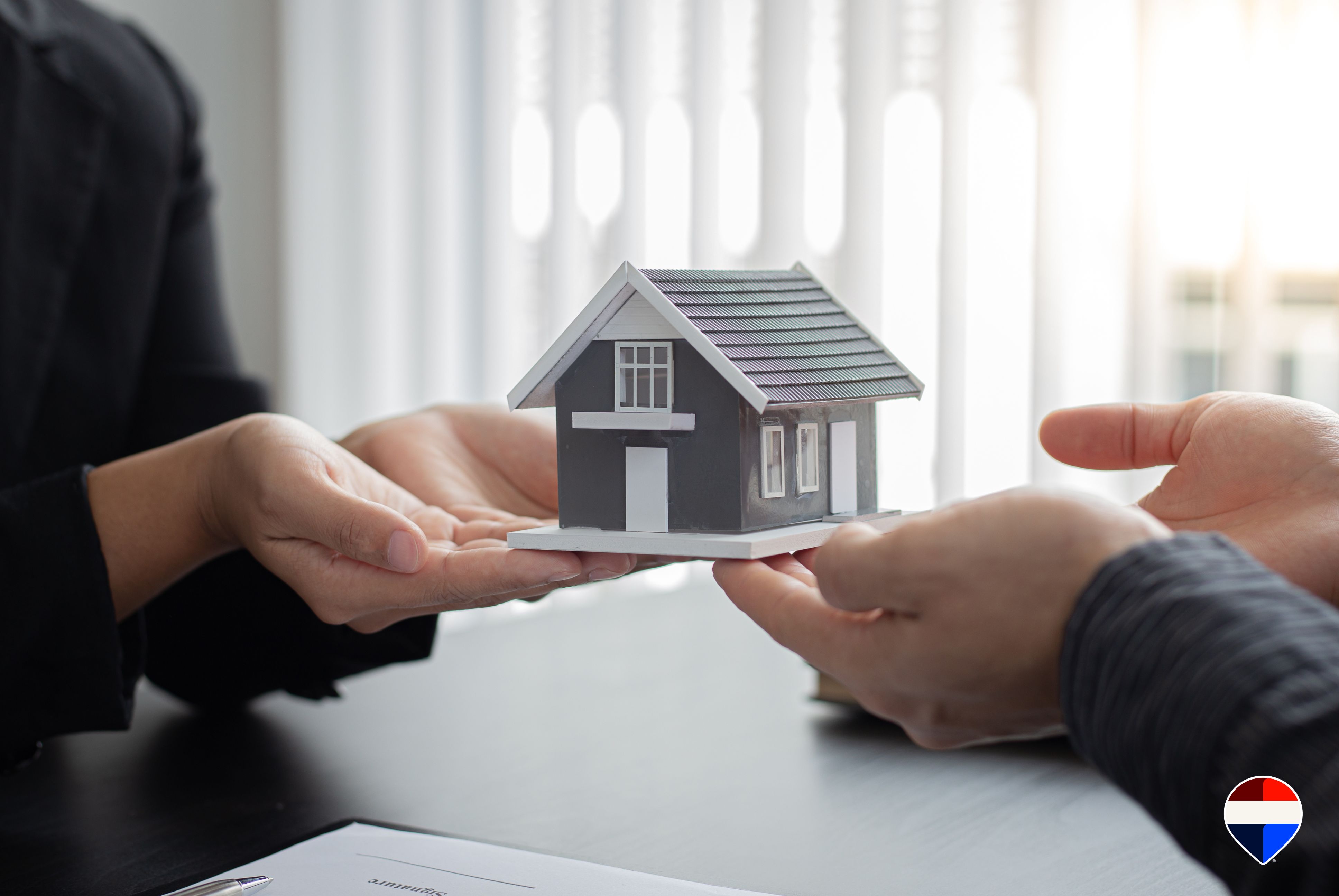 Modellino di casa che passa dalle mani dell'agente immobiliare a quelle dell'acquirente sopra il contratto di vendita