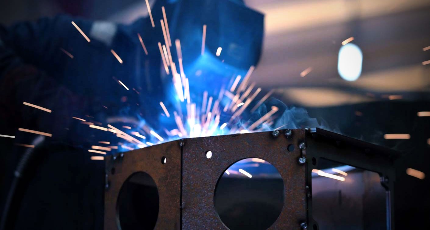 Close-up of a welder working on a metal structure with visible sparks.