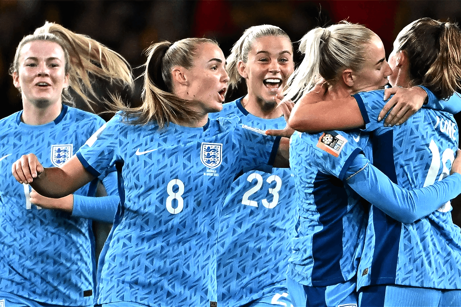 A group of female football players in blue jerseys celebrate joyfully together on the field.