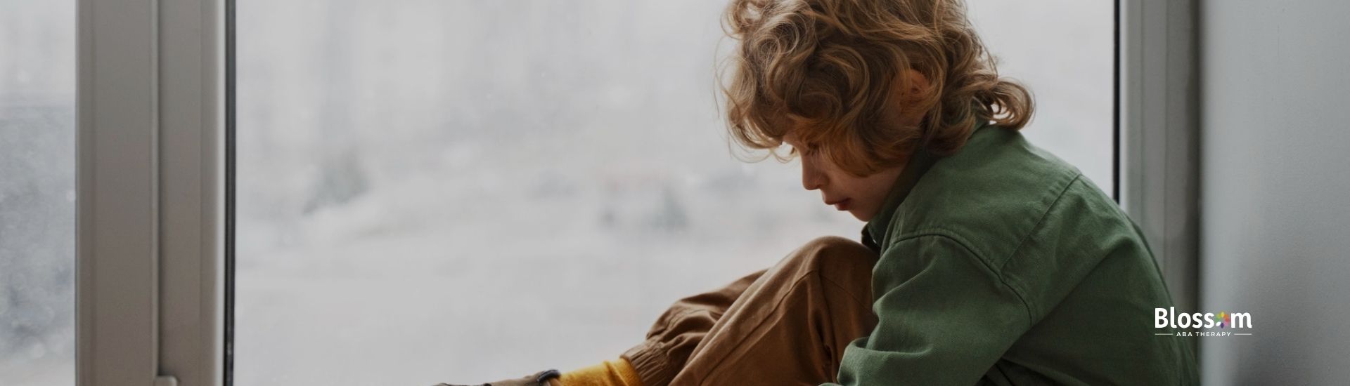 Child sitting by window playing with toy car on wooden floor.