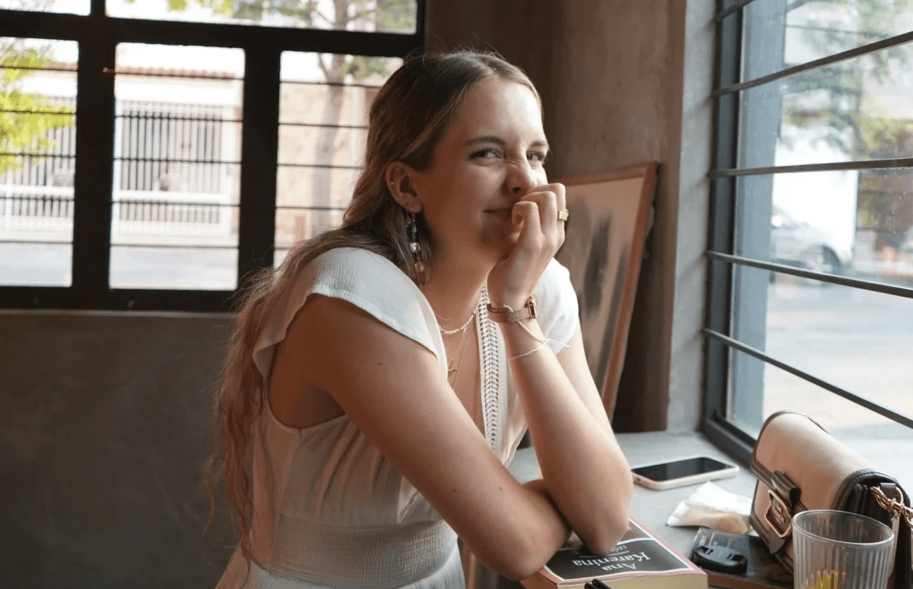 A model wearing an elegant cream blazer sits on a chair against a bright blue background, showcasing a modern and minimalist professional style.