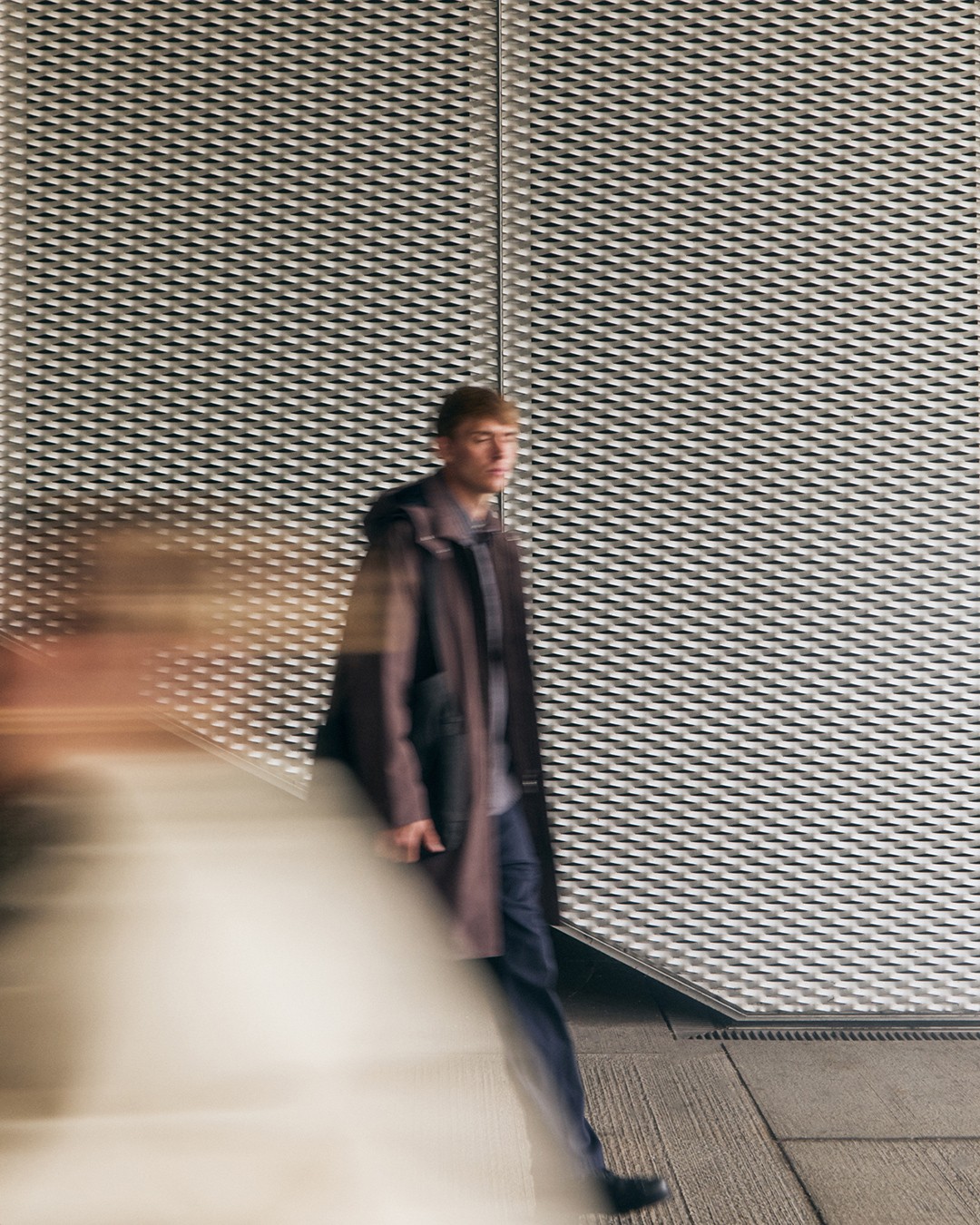 Un homme marche vêtu d'une parka technique marron dans le lookbook Norse Projects