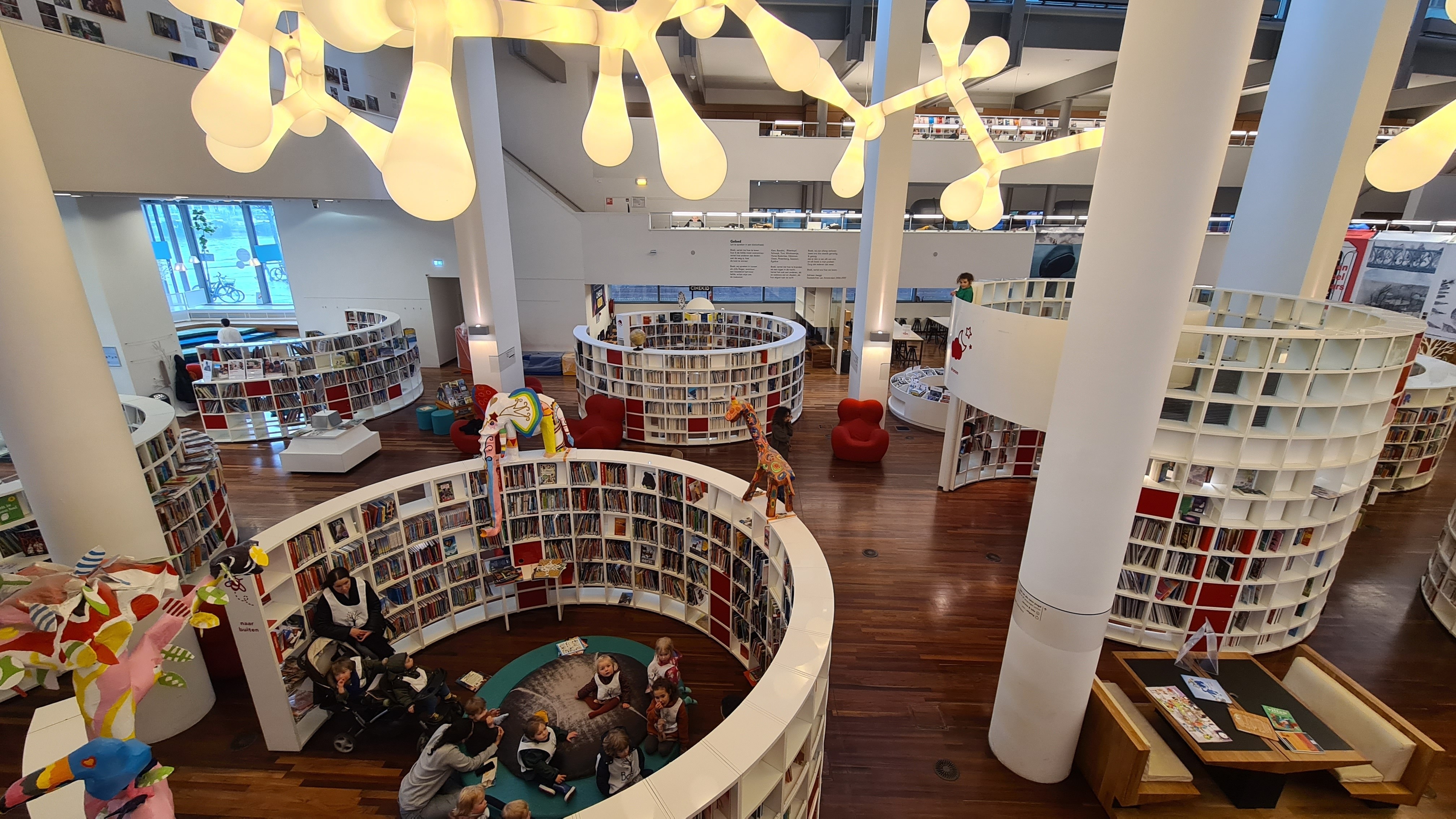 Inside of the OBA library at Oosterdock, showcasing curved shelves full of books beneath sculptural lighting.