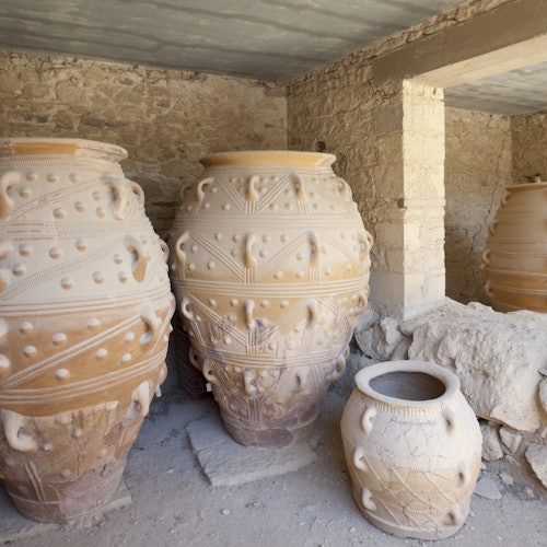 Three large, intricately patterned ceramic pots and one smaller pot are placed in a rustic stone building with exposed beams.