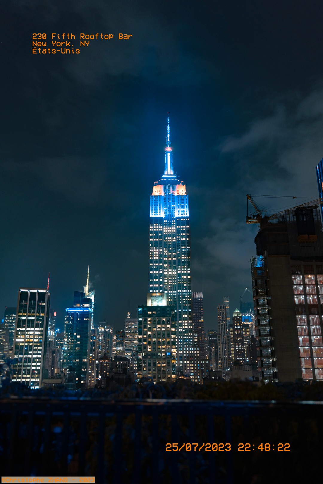Vue nocturne de l'Empire State Building illuminé en bleu depuis le 230 Fifth Rooftop Bar.