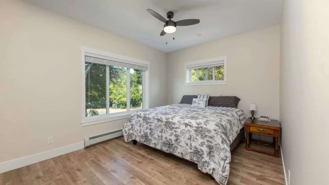  Spacious master bedroom in Vancouver custom home with large windows, ceiling fan, premium hardwood flooring, and soft neutral tones providing natural light and comfort