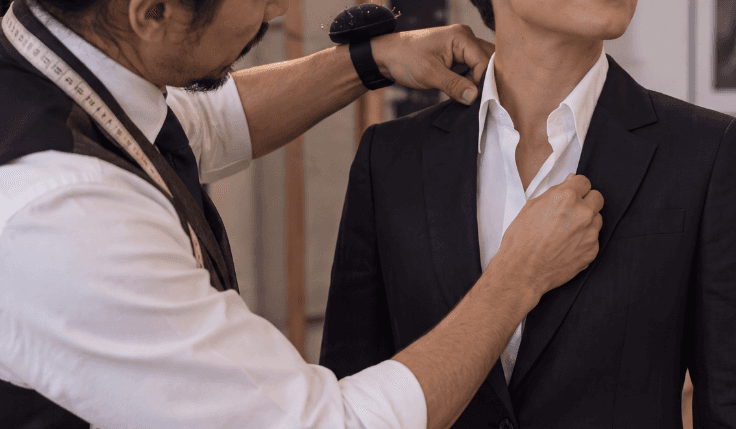 Tailor adjusting a made-to-measure shirt and custom suit jacket during a fitting