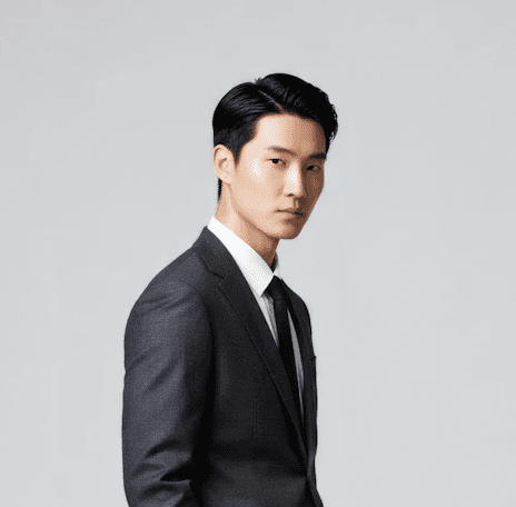 Man with dark hair wearing charcoal suit and black tie, professional headshot