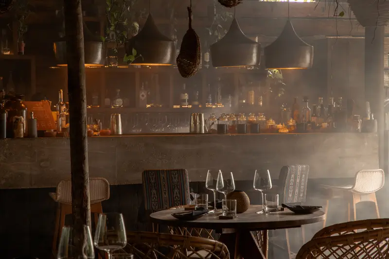 El área del bar bien iluminada y armoniosa del restaurante Ocumare con botellas de licor en estantes y mesa de comedor con sillas para los invitados.