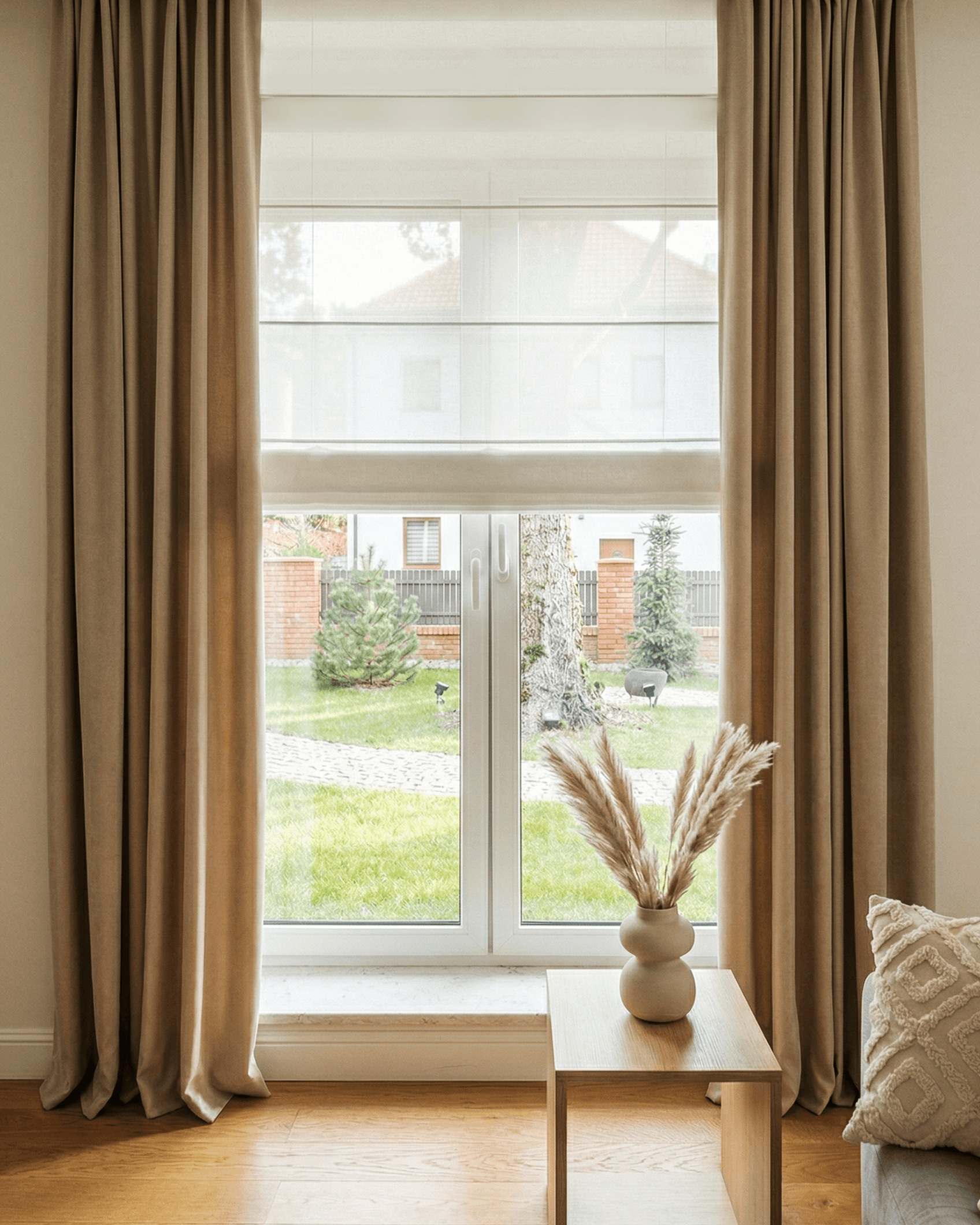 Beżowe rolety rzymskie połączone z długimi, mięsistymi zasłonami w eleganckim salonie. HeyShade Pruszków – kompleksowe aranżacje okienne na wymiar.
