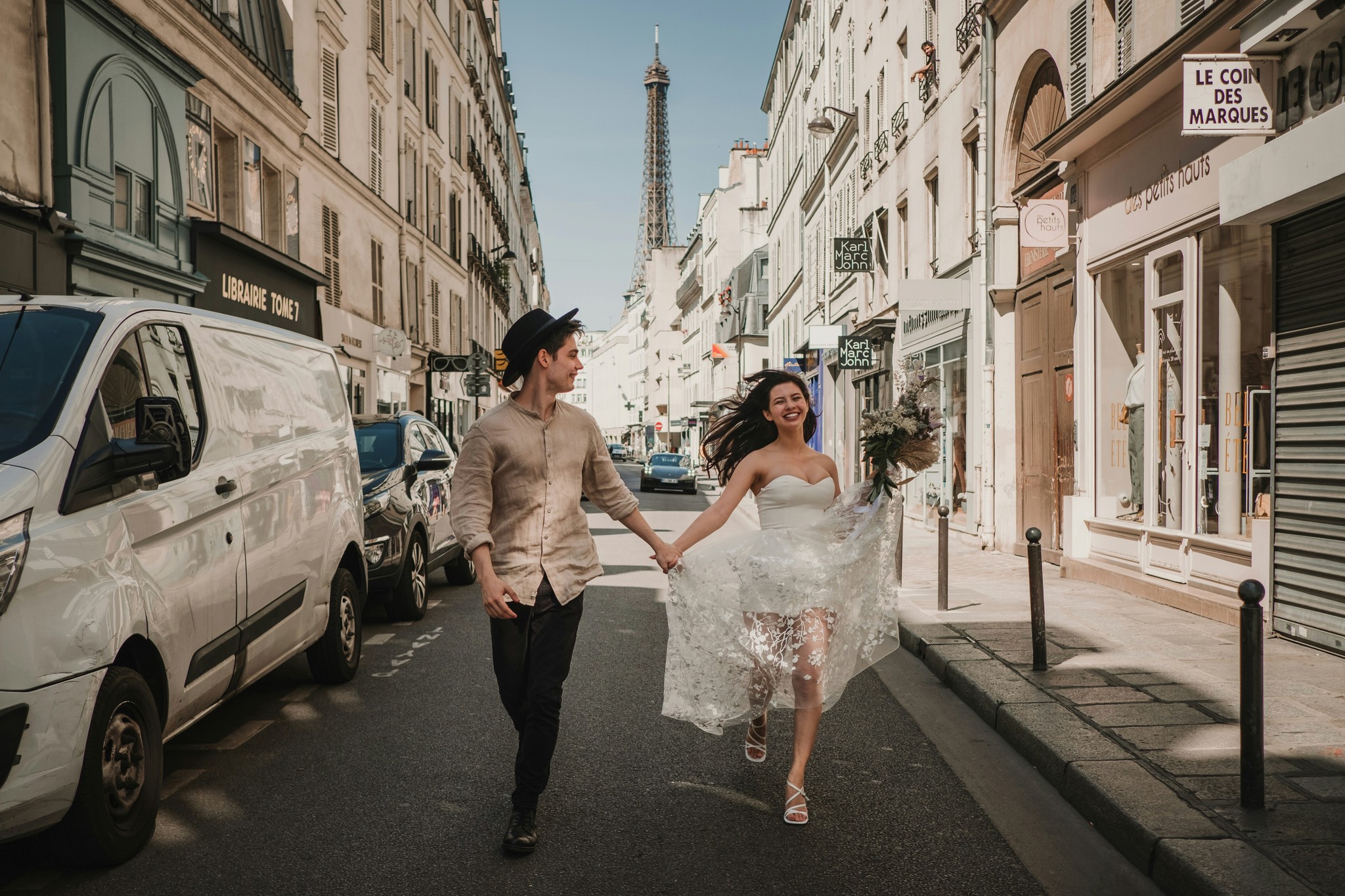 Couple running hand in hand down a Parisian street with the Eiffel Tower visible in the background and the bride's dress flowing in the wind