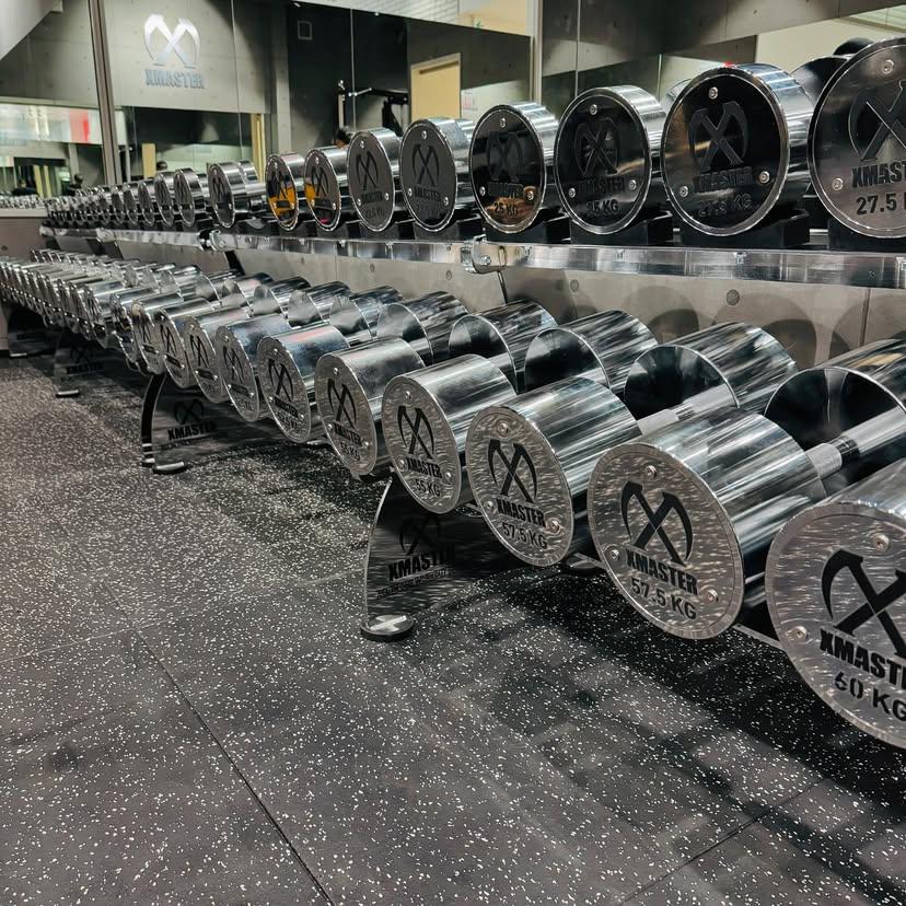 Two individuals are working out in a gym, focusing on dumbbells and strength training equipment.
