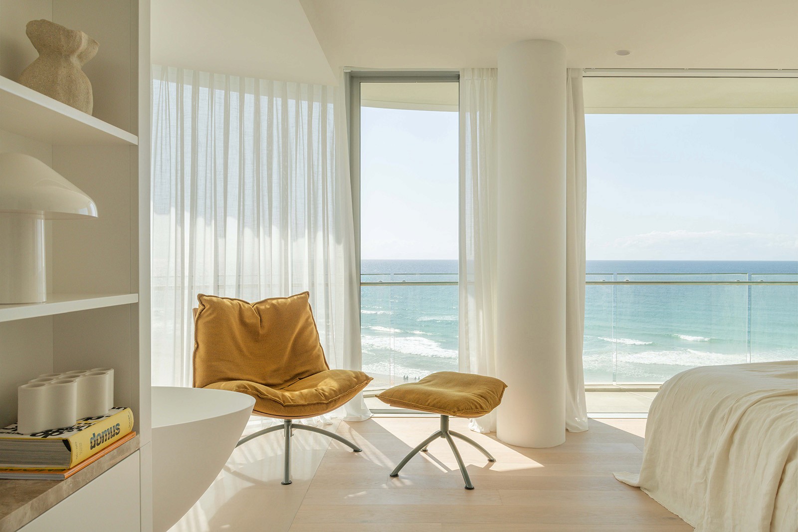High Tide apartment bedroom with ocean-facing windows, relaxed lounge chair, and soft coastal interior overlooking Surfers Paradise beach.
