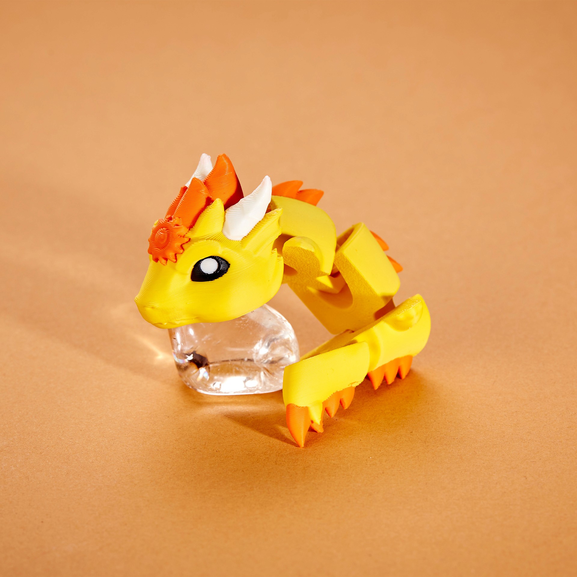 A vibrant yellow and orange 3D-printed dragon figurine with intricate details and a segmented body rests on a warm brown background.