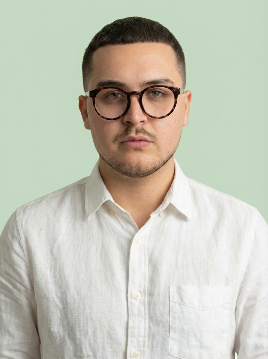 Close-up portrait of a freckled woman with soft pink hair and star earring, natural light, white tank top.