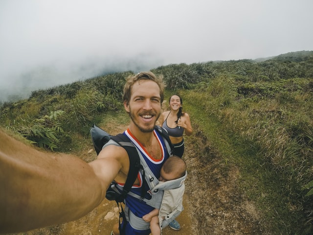 A person takes a selfie while running on a trail with lush greenery, surrounded by misty mountains.