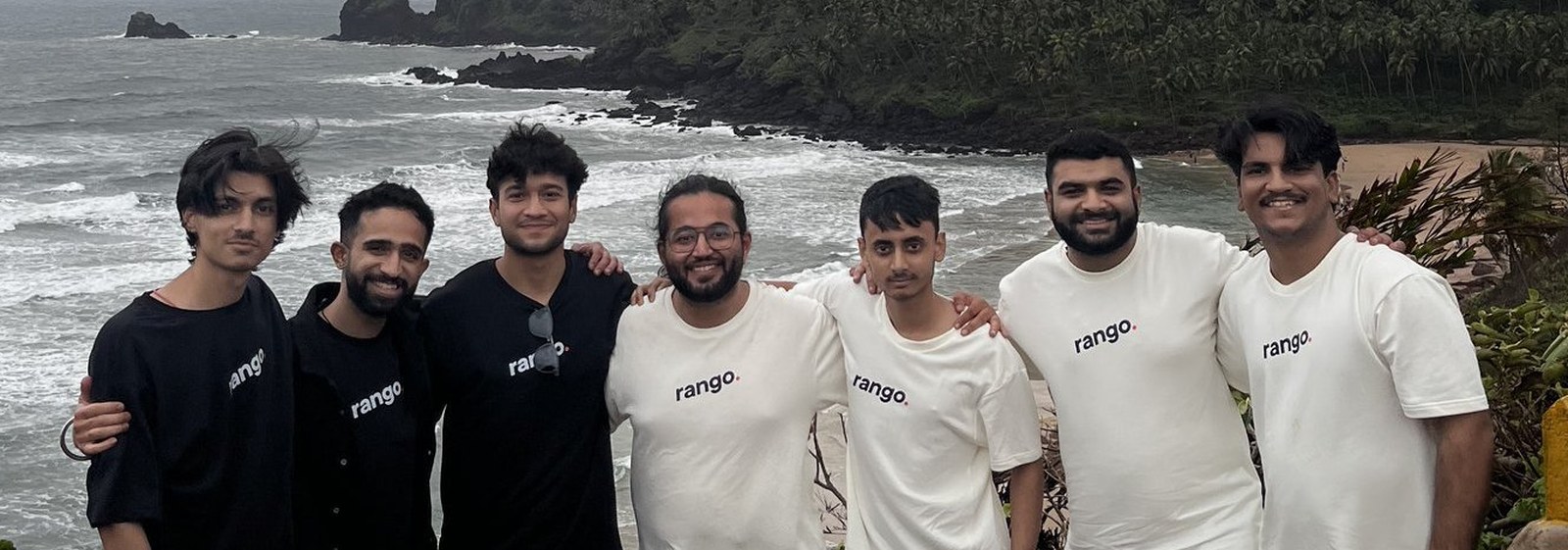 Seven members of the Rango team in Rango t-shirts on a clifftop above the sea in Goa