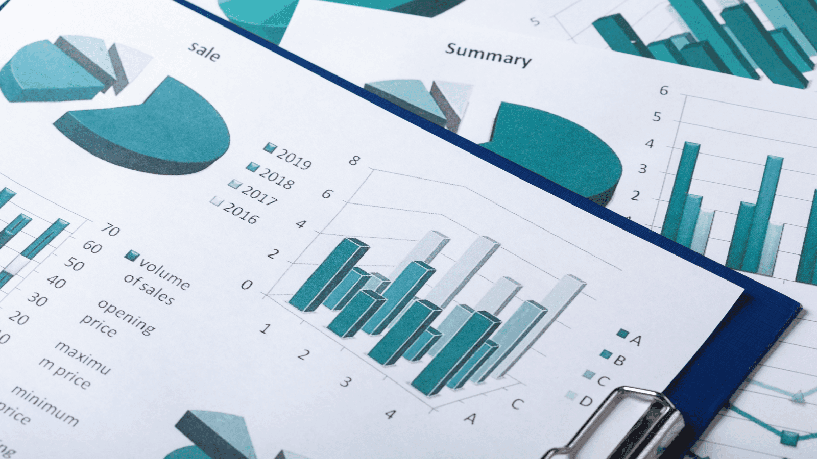 Financial reports and bar charts on a clipboard showing sales volume and summary data in teal and blue tones