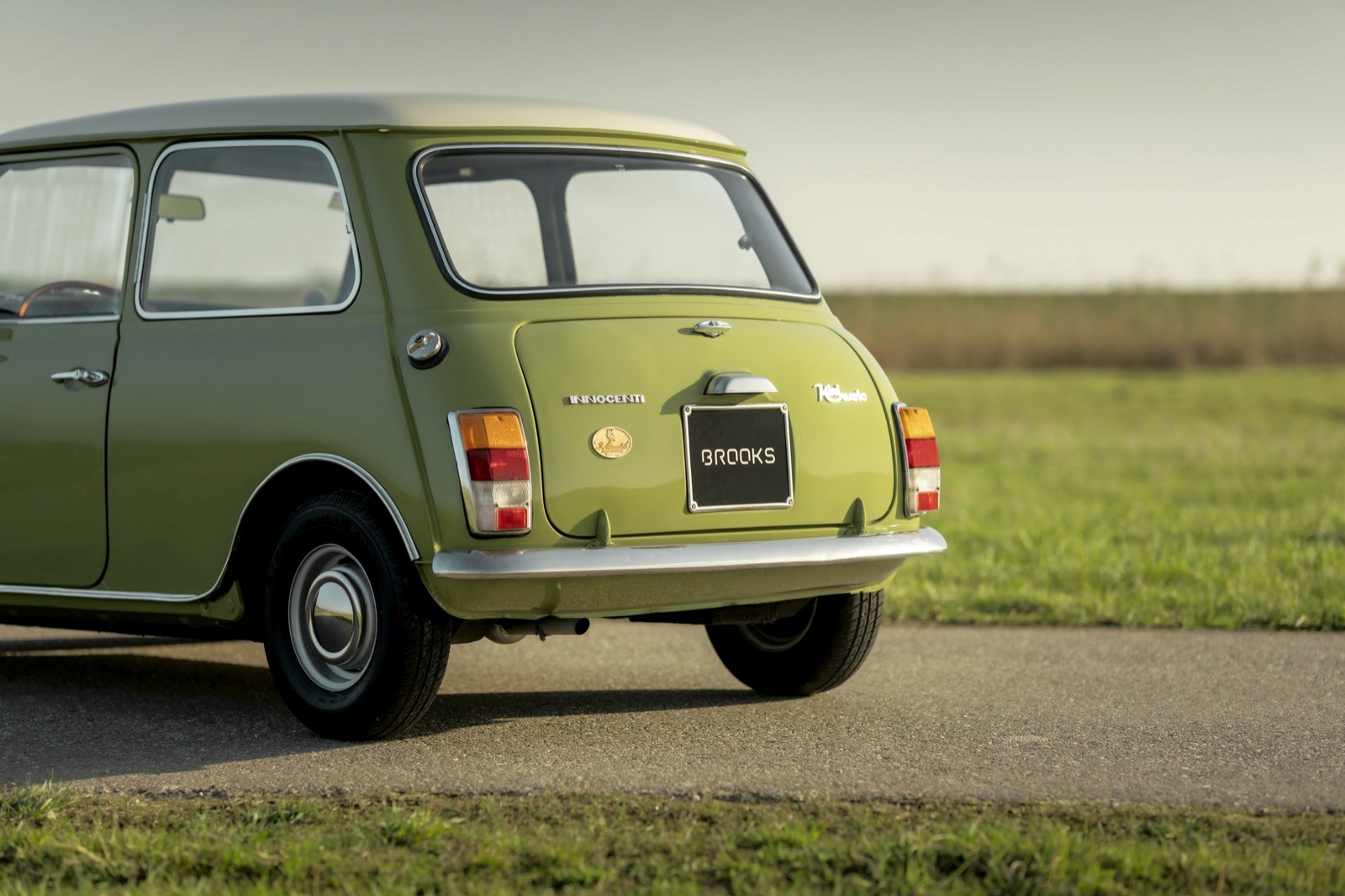 A green vintage car parked on a grassy area, with a clear sky in the background.