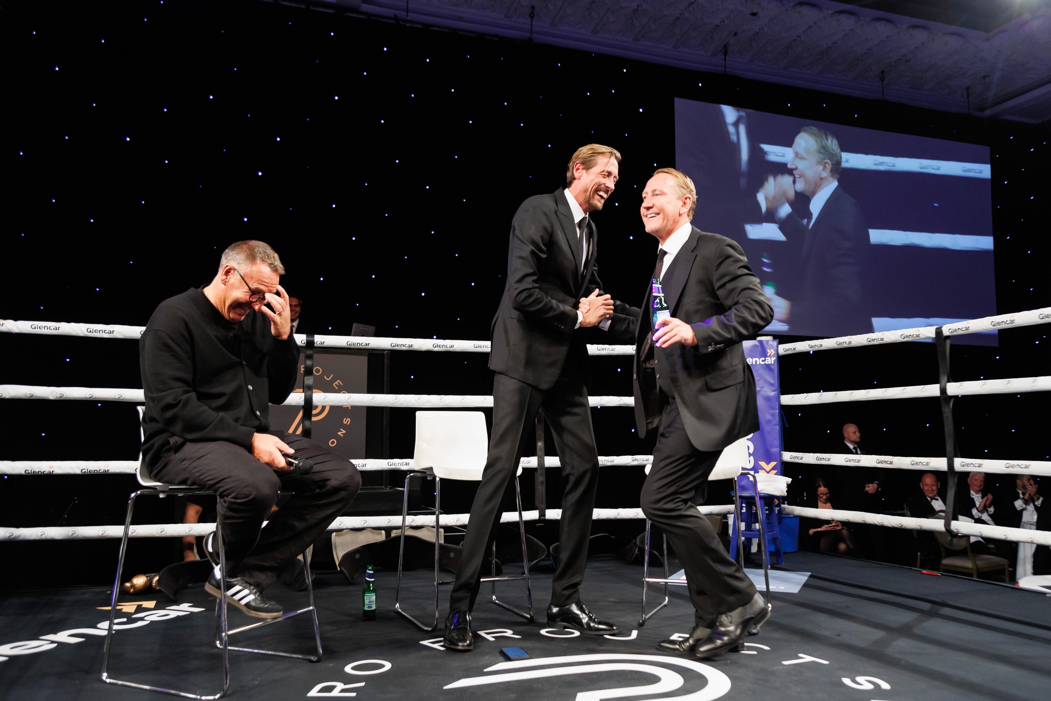 person discussing while standing in front of a large screen in front of people inside dim-lighted room