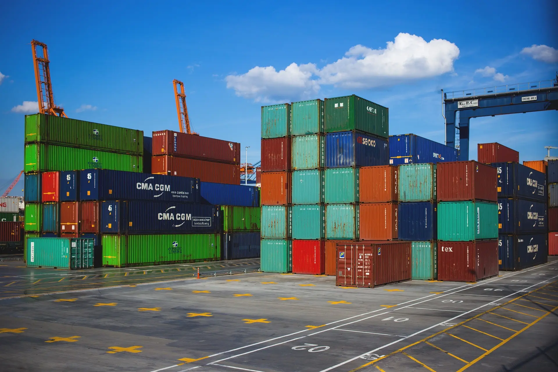 Stacked shipping containers at a busy port with cranes, awaiting UK customs clearance