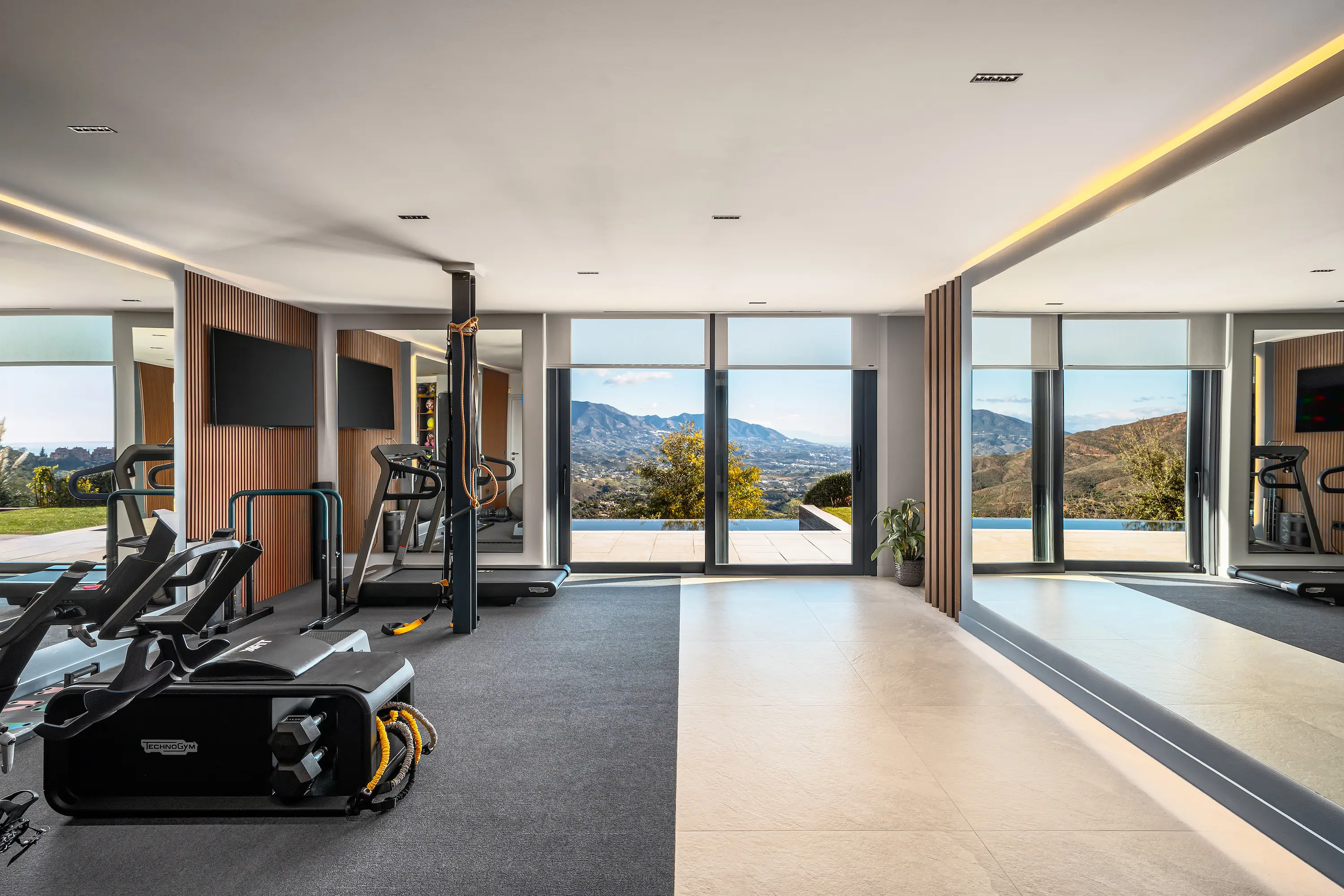 Villa Vista Marbella home gym with cardio equipment, mirrored wall, and mountain-view glazing