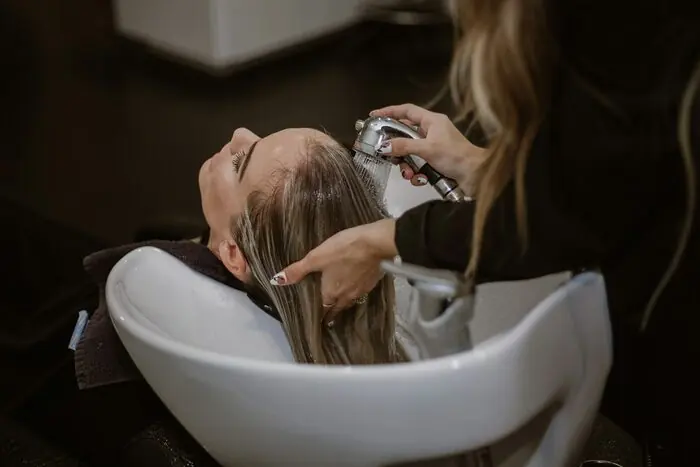 A client leaning back at a salon basin while a stylist washes her hair