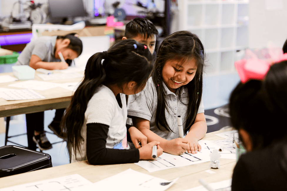 Two elementary students smiling, working on a project assigned by their eLab instructor.
