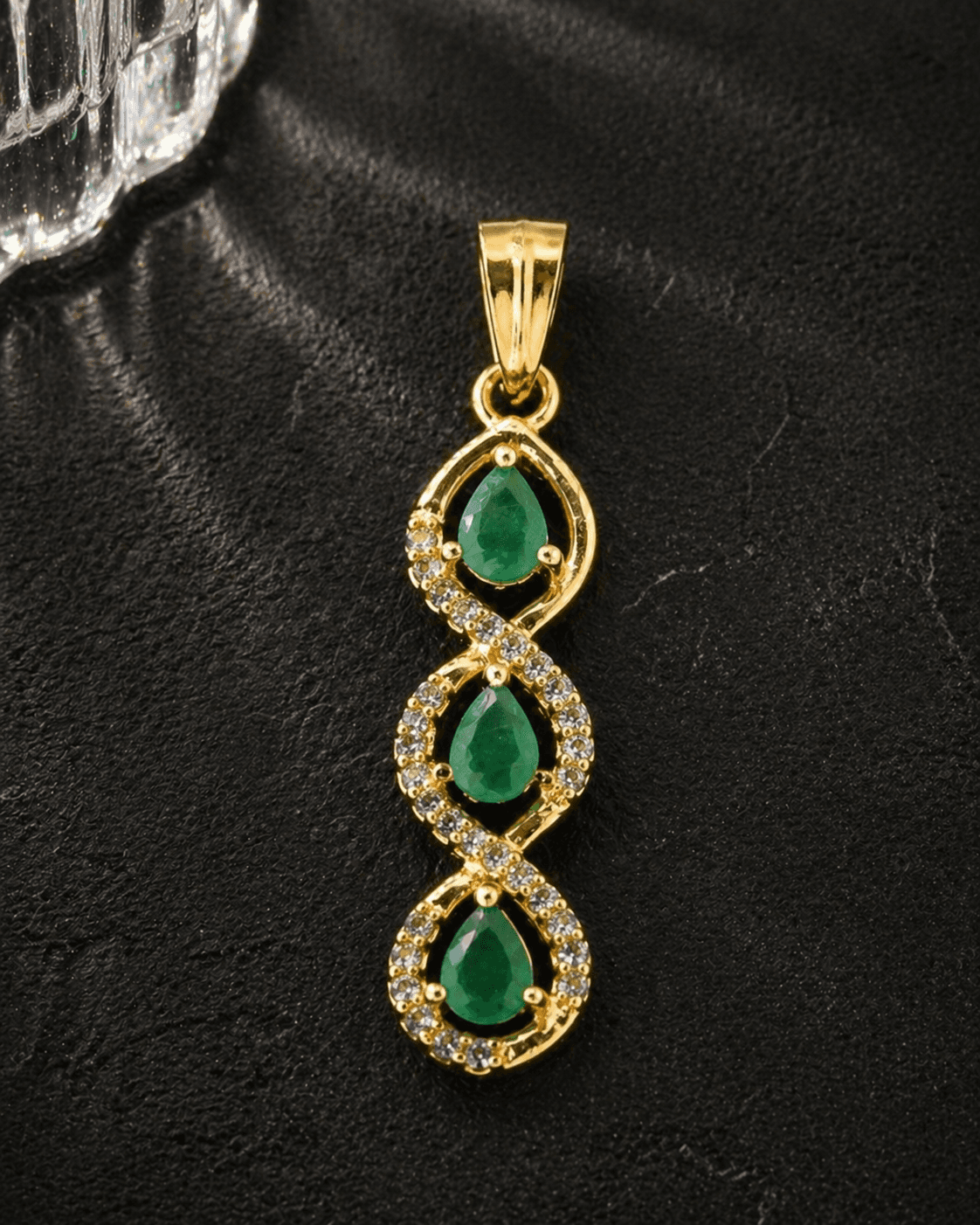 Gold pendant with three pear-shaped emeralds set in a twisted design, accented with small diamonds.