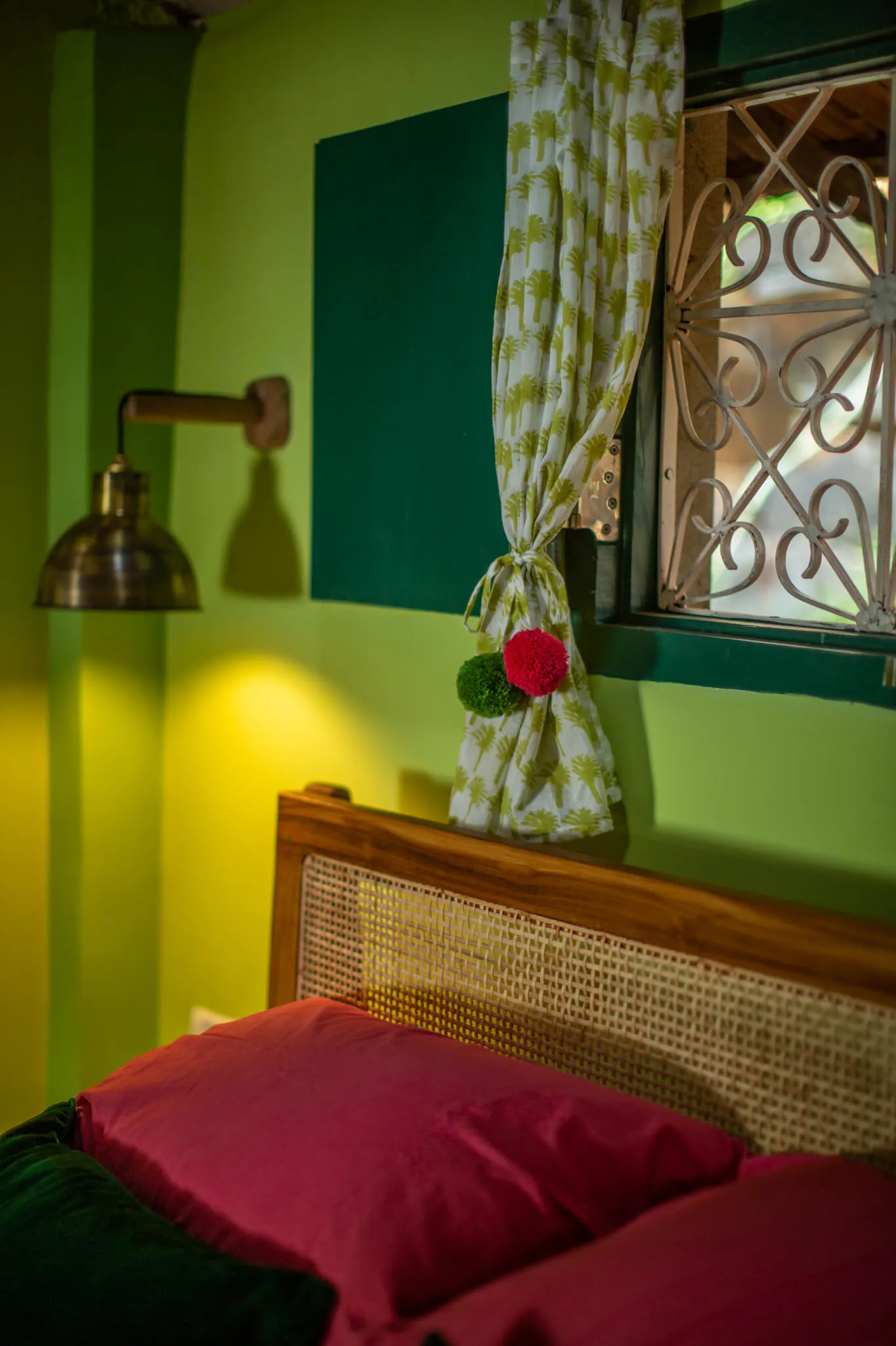 Cane bedhead and brass reading lamp in a green bedroom at Casa Jaali