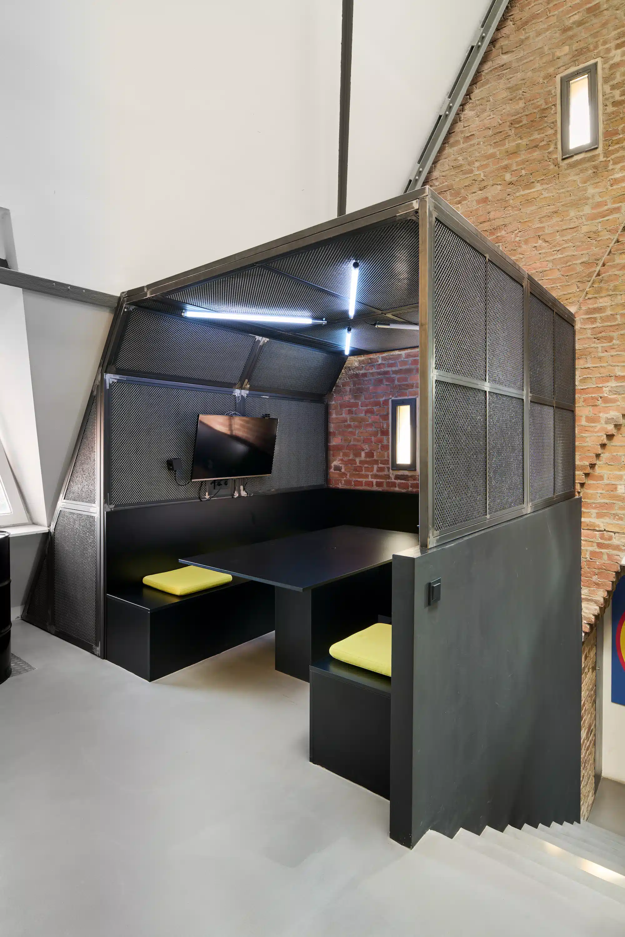 Dojo Office – private meeting pod made of black steel grid with yellow seat cushions and built-in screen