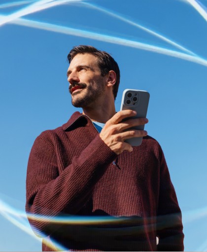 A professional man using a smartphone outdoors under a clear blue sky, demonstrating mobile time management for business and remote team productivity through flexible scheduling software.