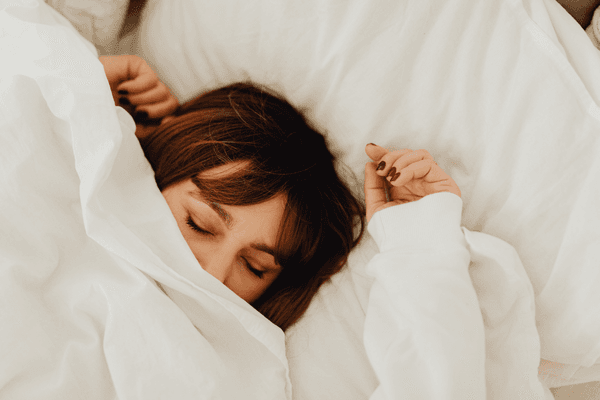 Image of a woman with brown hair sleeping under white covers in a bed