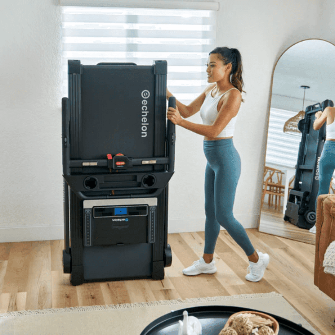 A woman folds up a treadmill so it is out of the way in her living room.