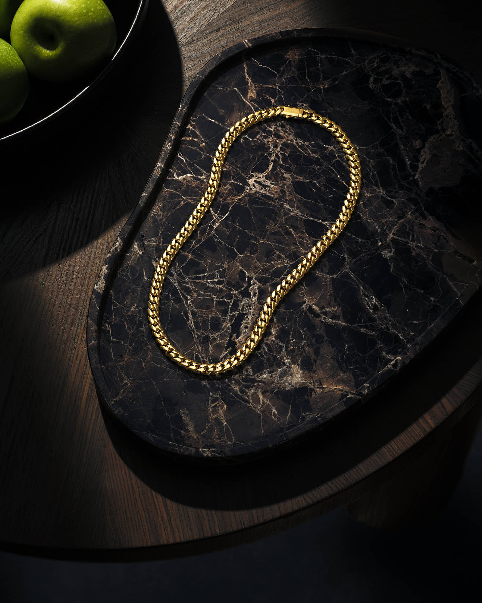 Gold chain necklace on dark marble tray, elegant jewelry display.
